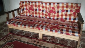 A wooden sofa with a checkered fabric and floral patterns, placed on a patterned rug.