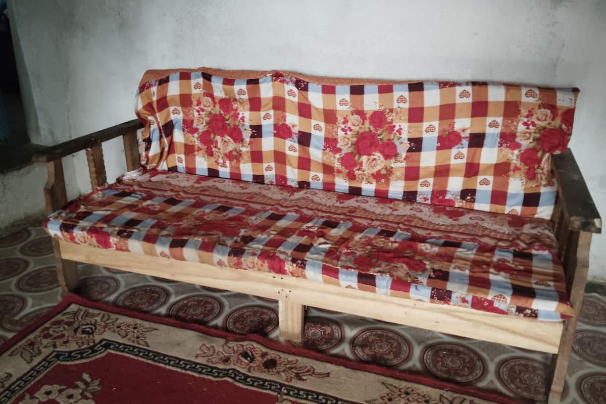 A wooden sofa with a checkered fabric and floral patterns, placed on a patterned rug.
