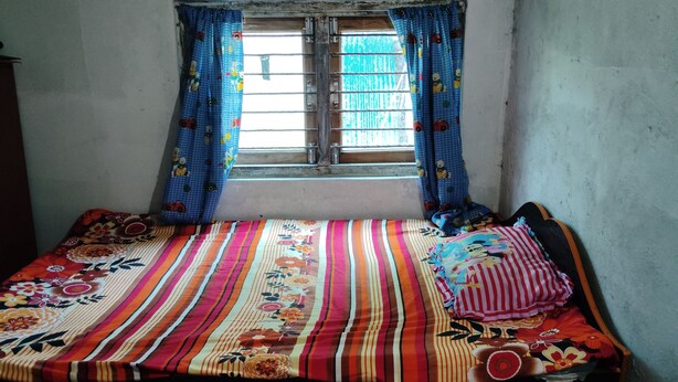 A small, simple room with a single bed, a window with curtains, and a plain wall.