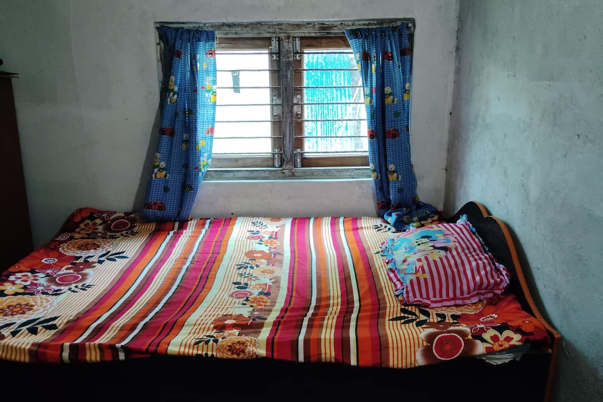 A small, simple room with a single bed, a window with curtains, and a plain wall.