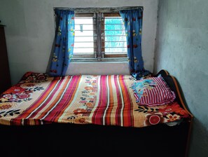 Een kleine, eenvoudige kamer met een enkel bed, een raam met gordijnen en een sobere muur.