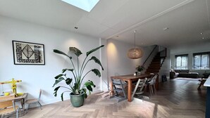 A spacious living area with a wooden herringbone floor, a dining table with chairs, a large potted plant, and a staircase leading to an upper level. - Heerlijk Ruim Familie Appartement Vlakbij de Jordaan (Amsterdam)