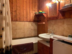 Ein Badezimmer mit Holzwandverkleidung, einer Badewanne, einem Waschbecken und einem Spiegel.