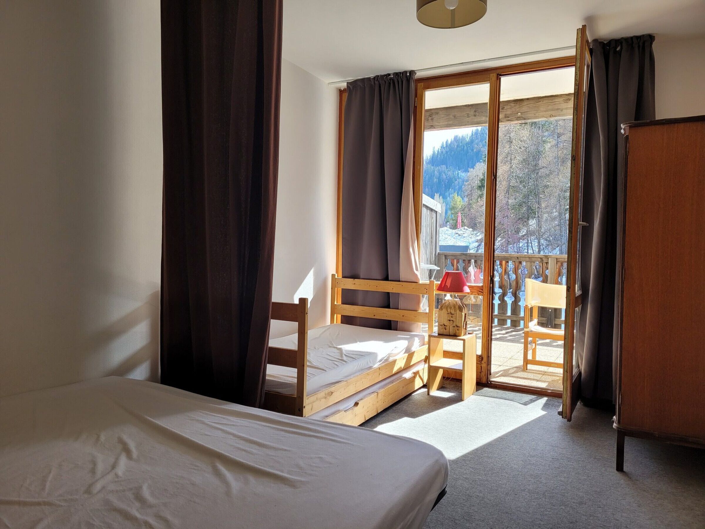 Un dormitorio con cama, una silla de madera, una mesita con lámpara y vista a un paisaje nevado a través de una puerta corrediza de vidrio.