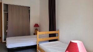 A small, neatly arranged bedroom with two single beds, a wooden headboard, a red lamp, and a wardrobe with a curtain. - Apartment 6 pers, South Terrace, Pra-Loup (Pra-Loup)