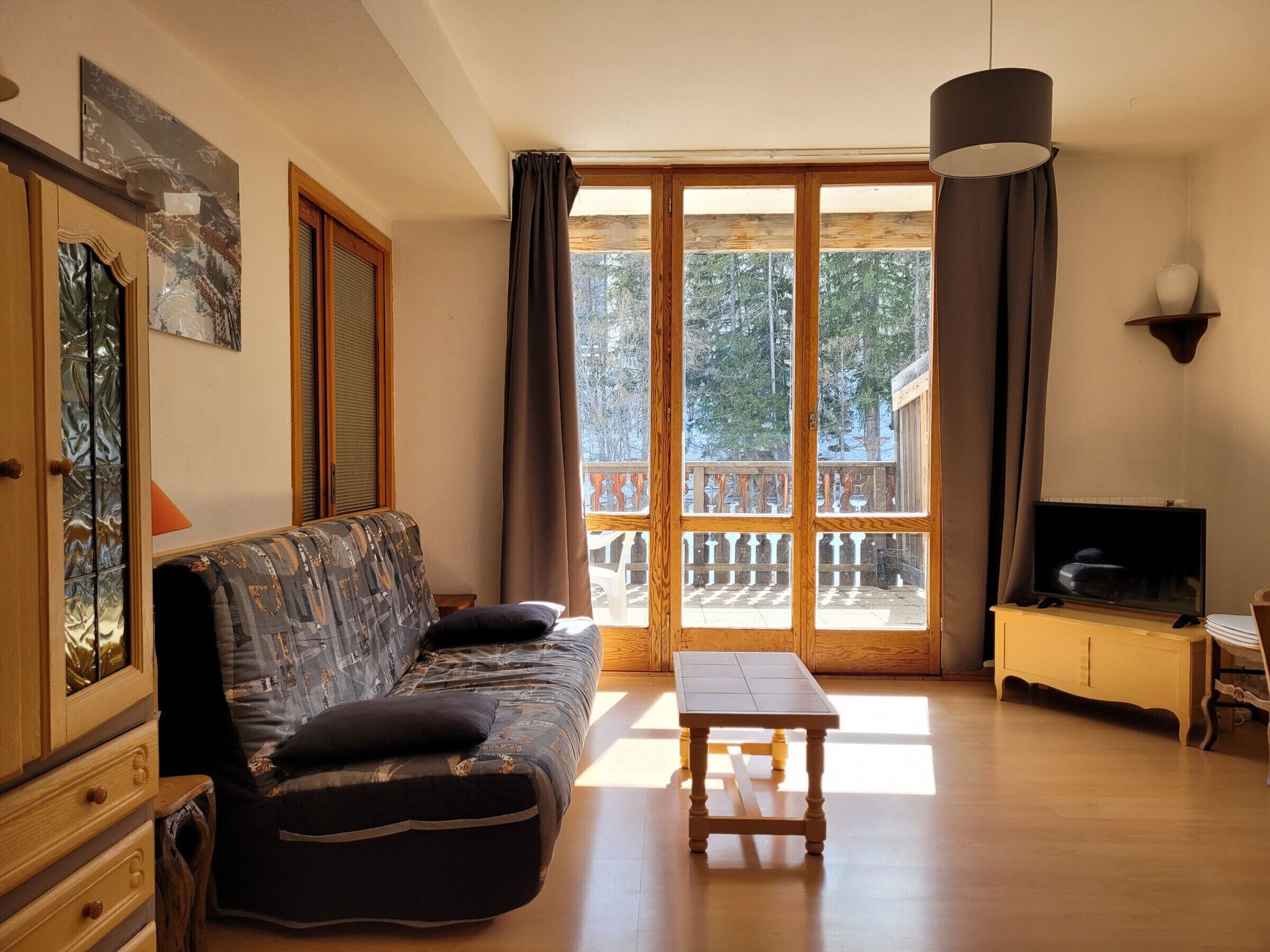 En stue med sofa, bord, fjernsyn og en balkon med gelænder.