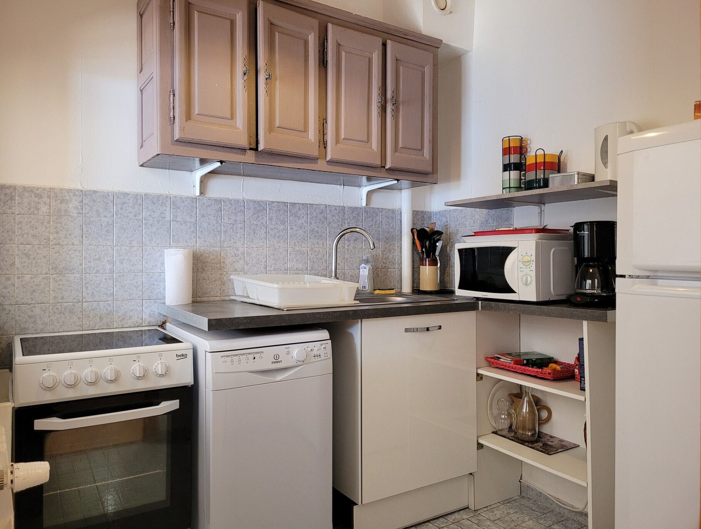 A compact kitchen with a built-in oven, microwave, dishwasher, and a sink with a faucet.