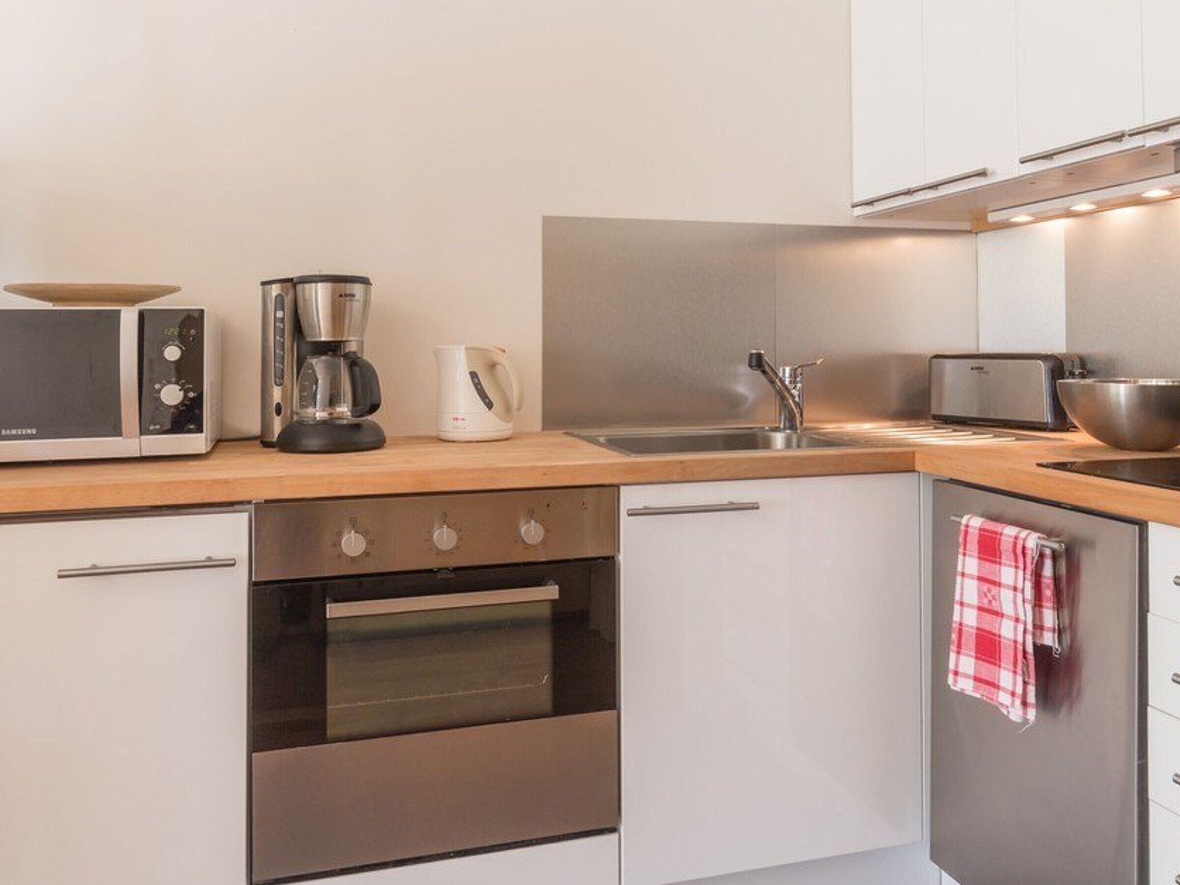 A modern kitchen with a microwave, coffee maker, toaster, sink, and oven.