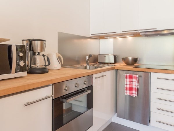 A modern kitchen with stainless steel appliances, a wooden countertop, and white cabinetry.