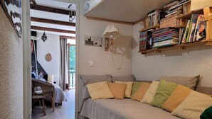 A cozy living room with a sofa, a bookshelf filled with books, a wall-mounted lamp, and a view of a balcony.