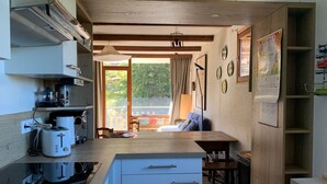A compact kitchen with a built-in stove, a coffee maker, and a toaster. There is a dining area with a table and chairs, and a large window providing a view of the outdoors.