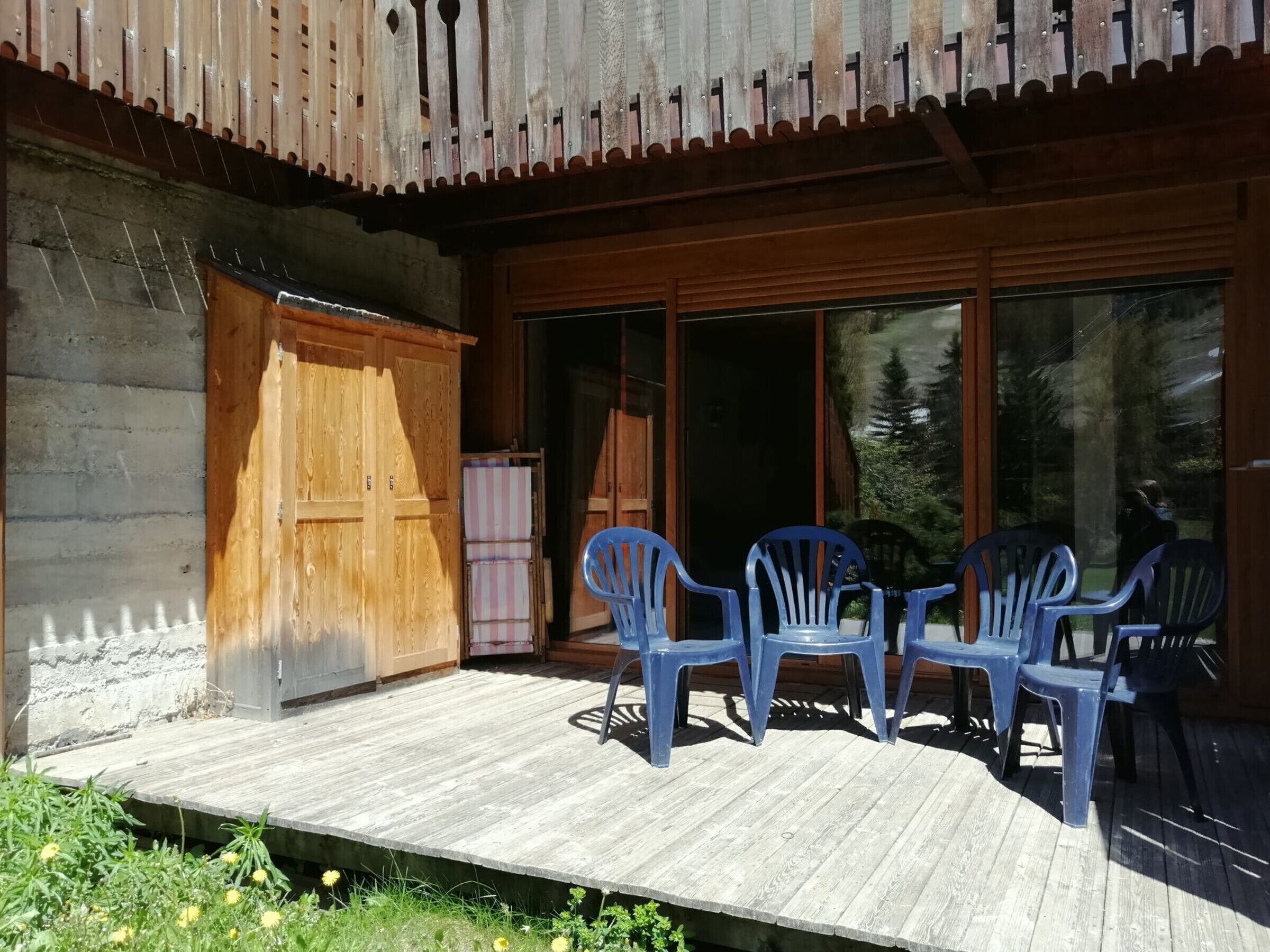 A wooden deck with plastic chairs, a wooden door, and a windowed entrance.