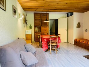 Uma sala de estar aconchegante com sofá, mesa de jantar e cadeiras, armários de madeira e teto de madeira.