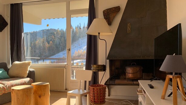 Un salon chaleureux avec une cheminée, un canapé, un téléviseur et une vue sur un paysage enneigé.