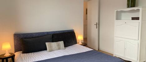 Ein Schlafzimmer mit einem Bett, zwei Nachttischlampen, einem Kleiderschrank und einer Tür.