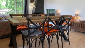 Un coin repas avec une table et des chaises en bois, un barbecue noir et un téléviseur.