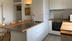 Une cuisine moderne avec des meubles blancs, un plan de travail en bois, un four encastré et un luminaire suspendu.
