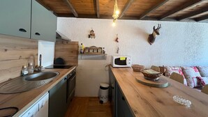 Kompakti keittiö, jossa on puukaapit, pesuallas, liesi ja mikroaaltouuni. Keittiössä on puinen työtaso, jonka päällä on kori ja pieni pöytä. Seinälle on ripustettu koristeena peuranpää.