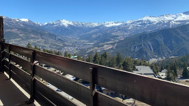 Vista de la montaña desde un balcón con baranda de madera, con vistas a montañas nevadas y un valle.
