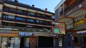 Un edificio de varios pisos con diversos comercios en la planta baja, incluyendo una discoteca, una farmacia y una tienda de deportes.