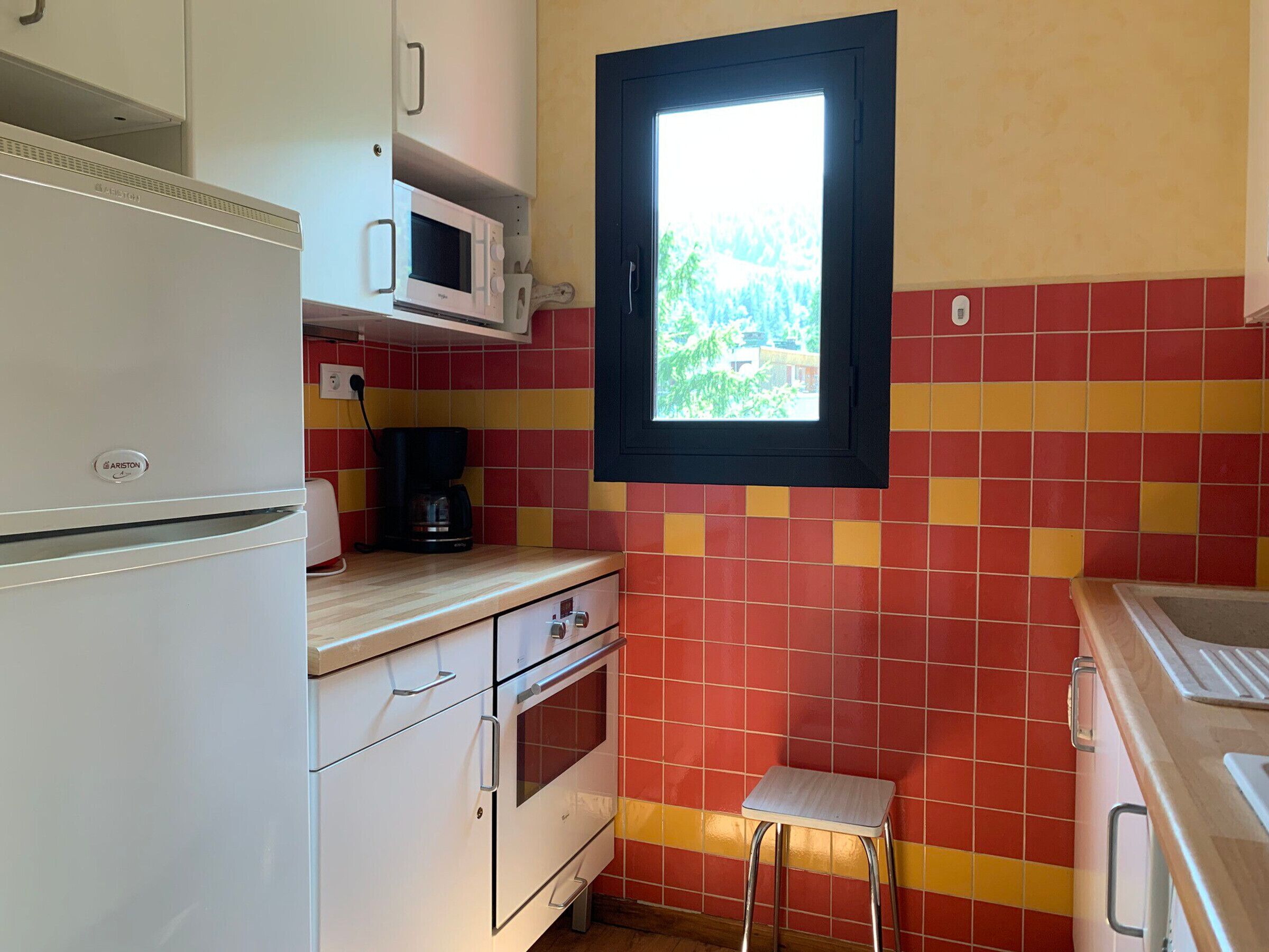 Una cucina compatta con un frigorifero bianco, un forno a microonde, una macchina da caffè e una finestra vista verde.