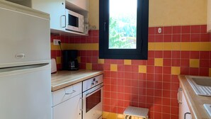 Una cocina compacta con un refrigerador blanco, un microondas, una cafetera y un ventanal con vista a áreas verdes.