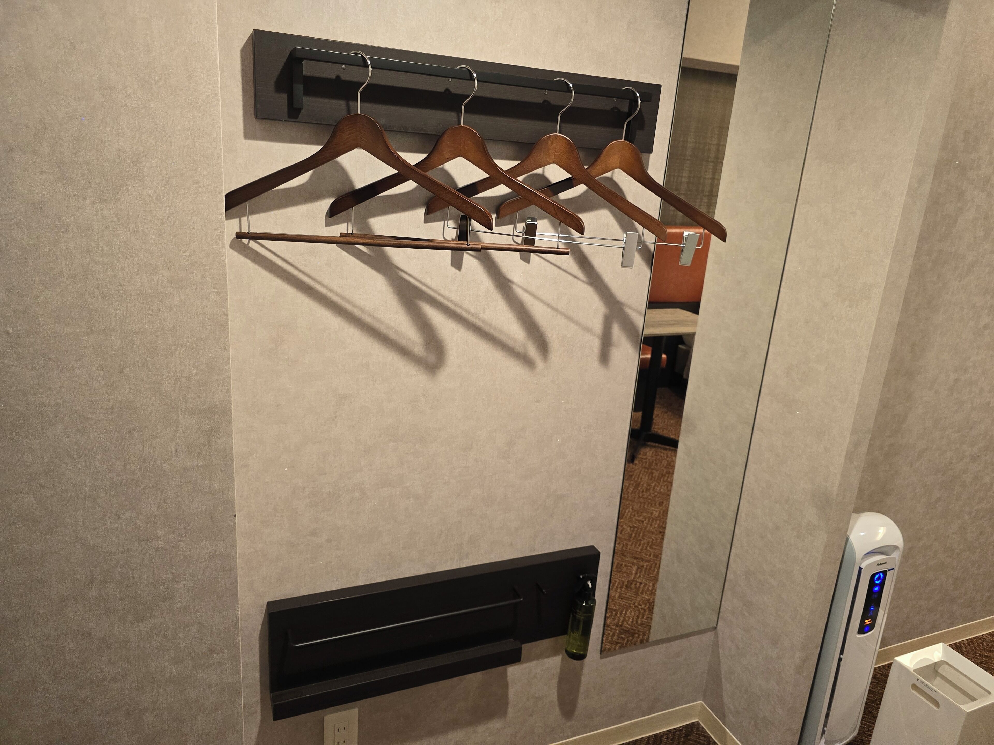 A wall-mounted drying rack with wooden hangers, a black shelf, and a white device, possibly a hand dryer, on a textured wall.