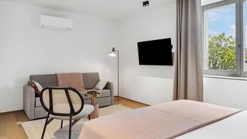 Una habitación de hotel moderna con una cama, un sofá, una silla, un televisor y una ventana con cortinas.