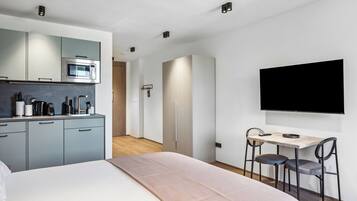 Una habitación de hotel moderna con kitchenette, una cama, un escritorio con dos sillas y un televisor montado en la pared.