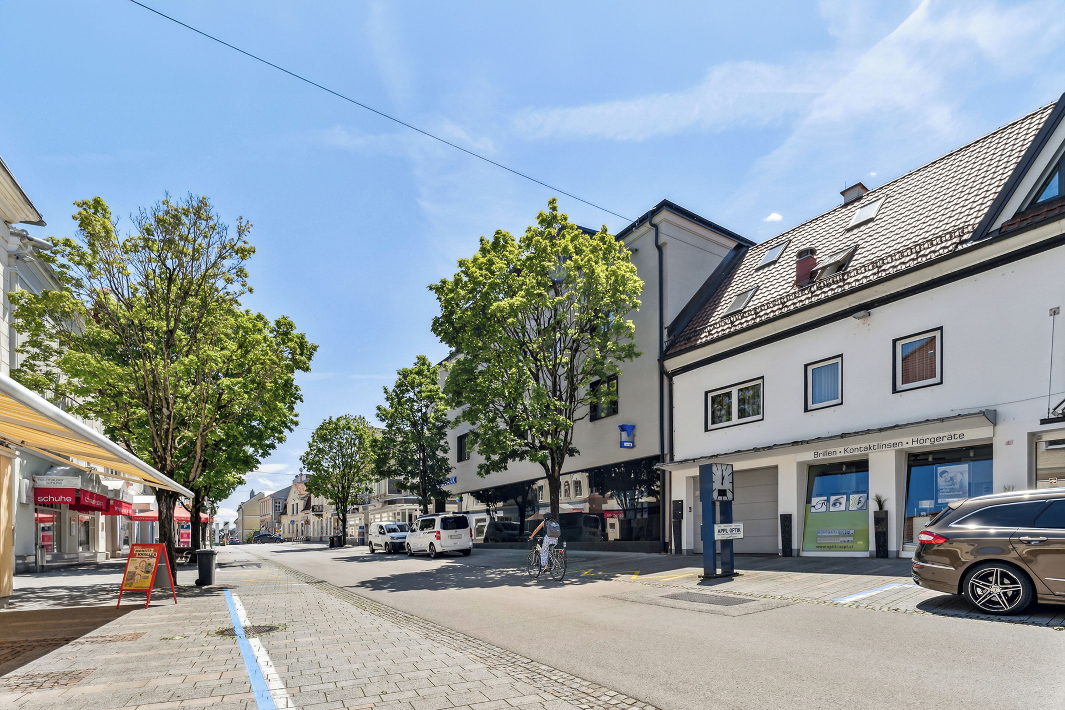 A street view with buildings, a cyclist, and parked cars.