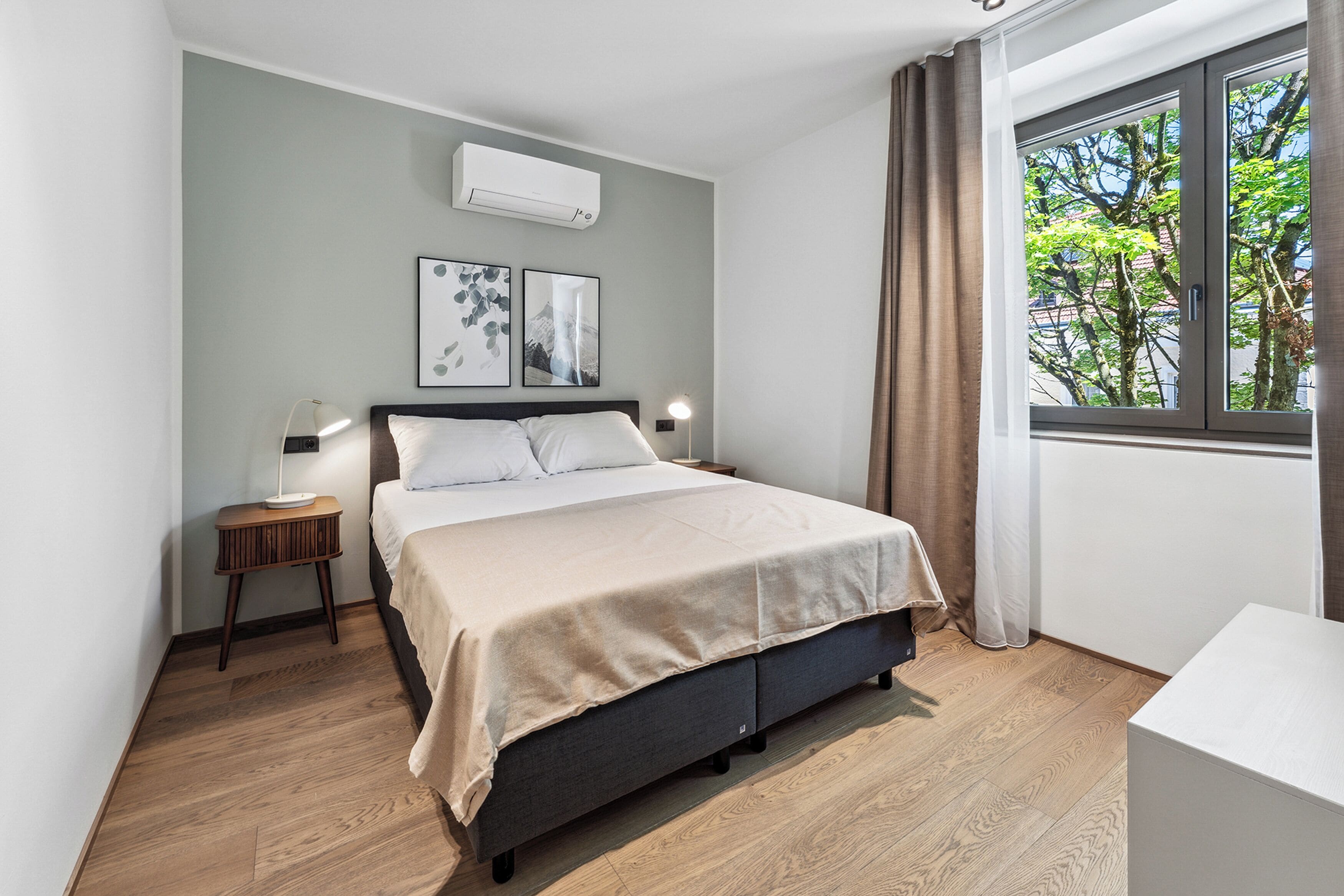 Una camera da letto con un letto, un comodino, una lampada, un condizionatore d'aria e una finestra con tende.