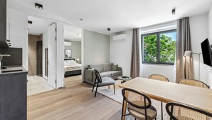 Habitación de hotel moderna con comedor, sofá y vistas a árboles por la ventana.
