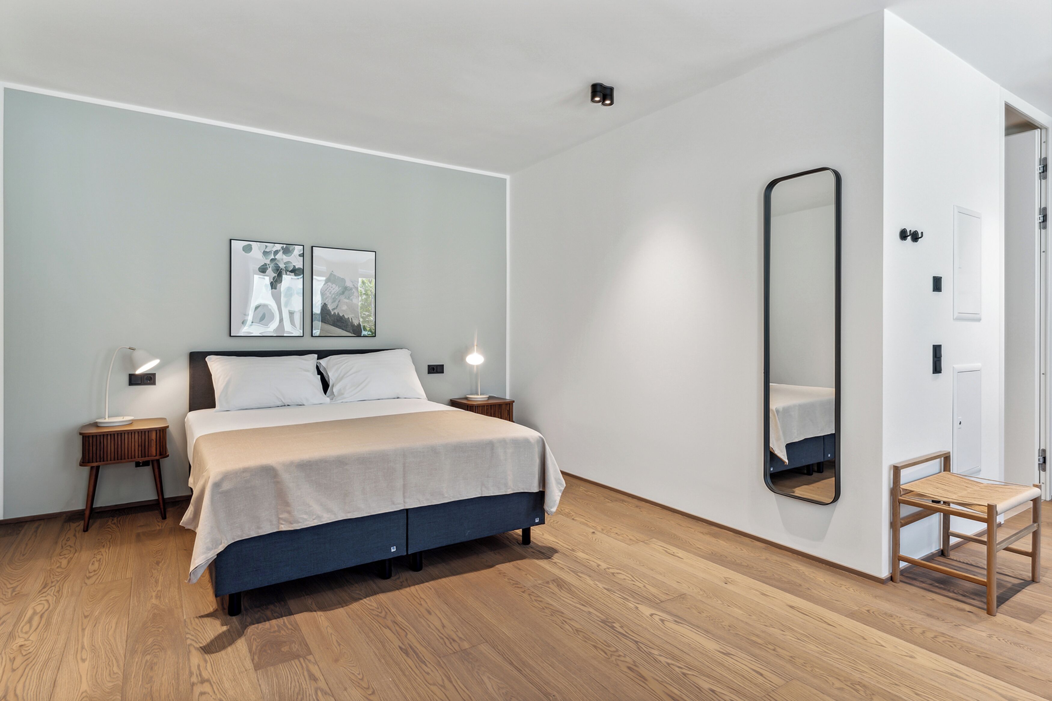 Une chambre à coucher moderne avec un lit, des tables de chevet, un miroir et des œuvres d’art accrochées au mur.
