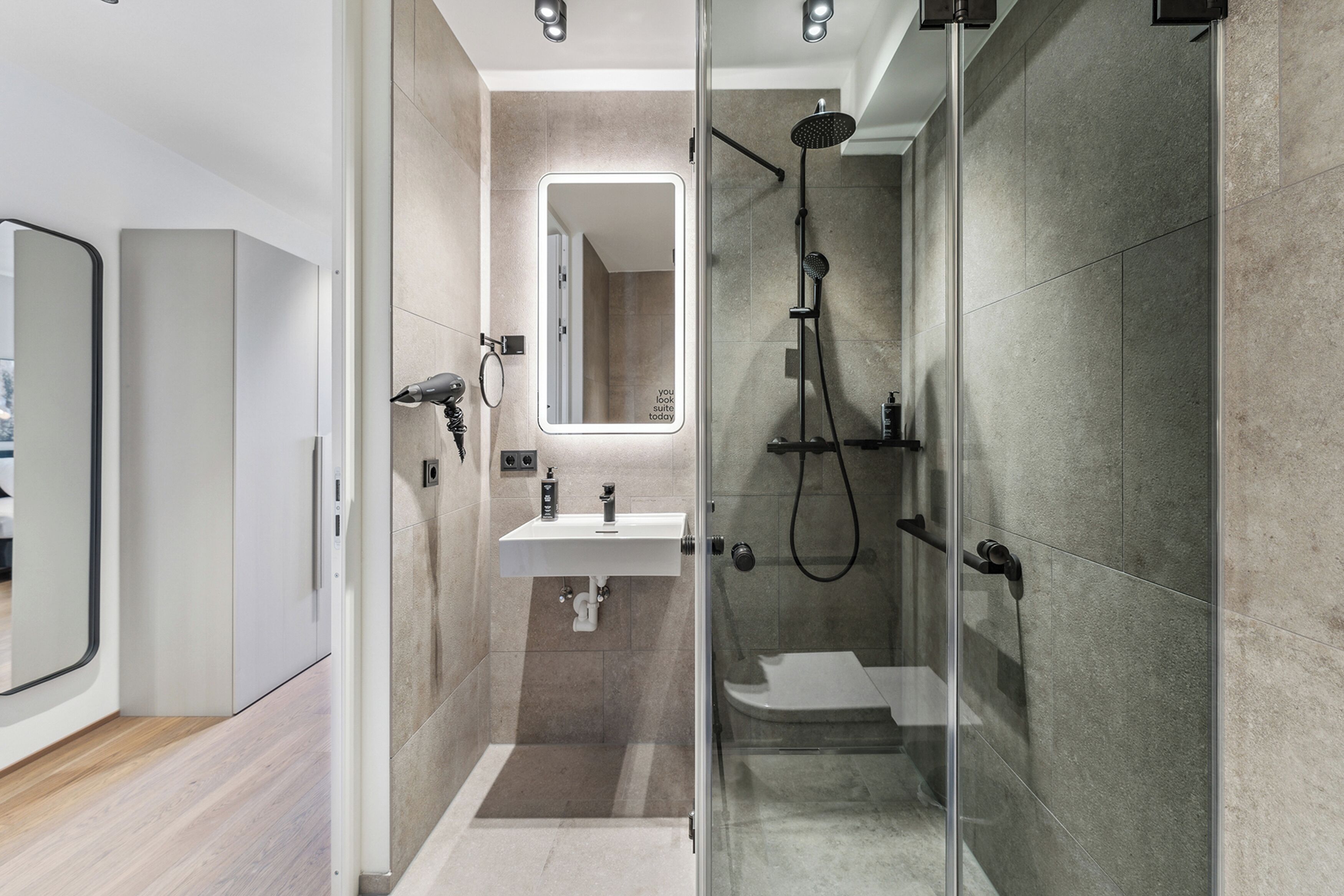 A modern bathroom with a glass-enclosed shower, a white sink, and a large mirror.