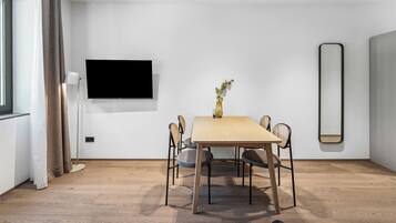 Un'elegante zona pranzo moderna con tavolo in legno, quattro sedie, un vaso con fiori, una TV a schermo piatto e un grande specchio a parete.