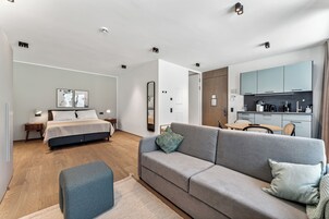 Un dormitorio moderno y bien iluminado con una cama grande, un sofá gris y una mesita pequeña.