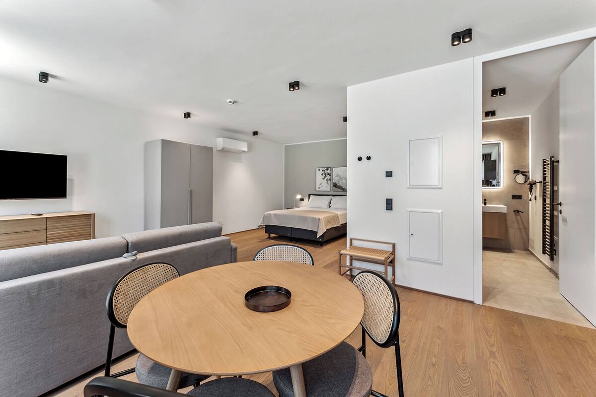 A modern, well-lit room with a sofa, a round dining table, and a bed.