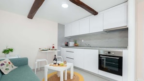 A modern kitchen with white cabinets, a built-in oven, and a small dining area with a table and chairs.
