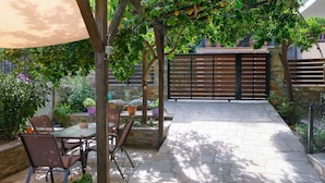 Ein Terrassenbereich im Freien mit Steinboden, Tisch und Stühlen sowie Topfpflanzen.