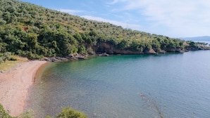 Eine Küstenlandschaft mit einem klaren Strand und einem mit Grün bewachsenen Hügel.