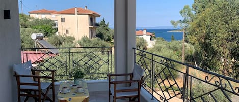 A balcony with two wooden chairs and a table, overlooking a residential area and a body of water.