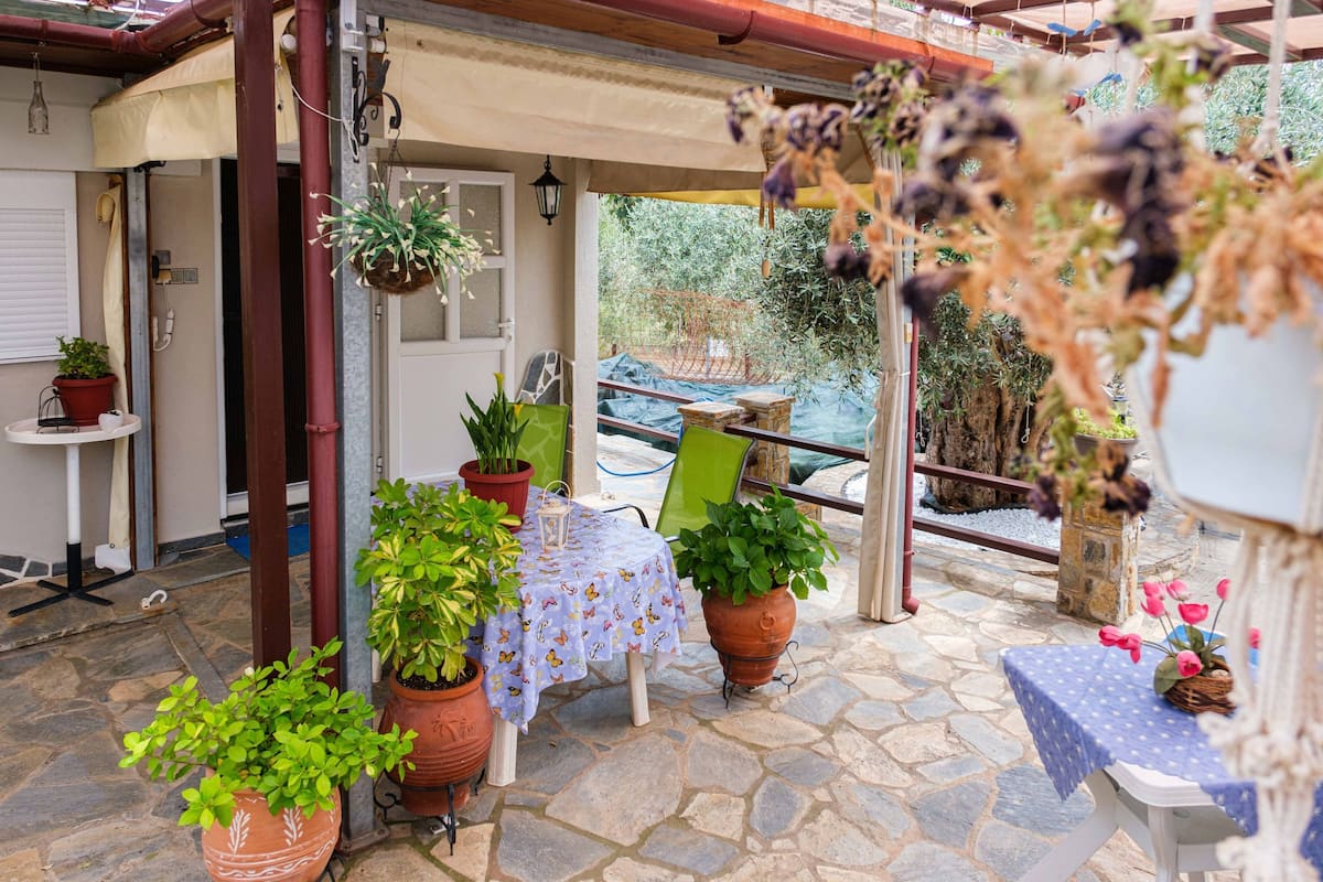 A patio with potted plants, a table with a tablecloth, and a chair.