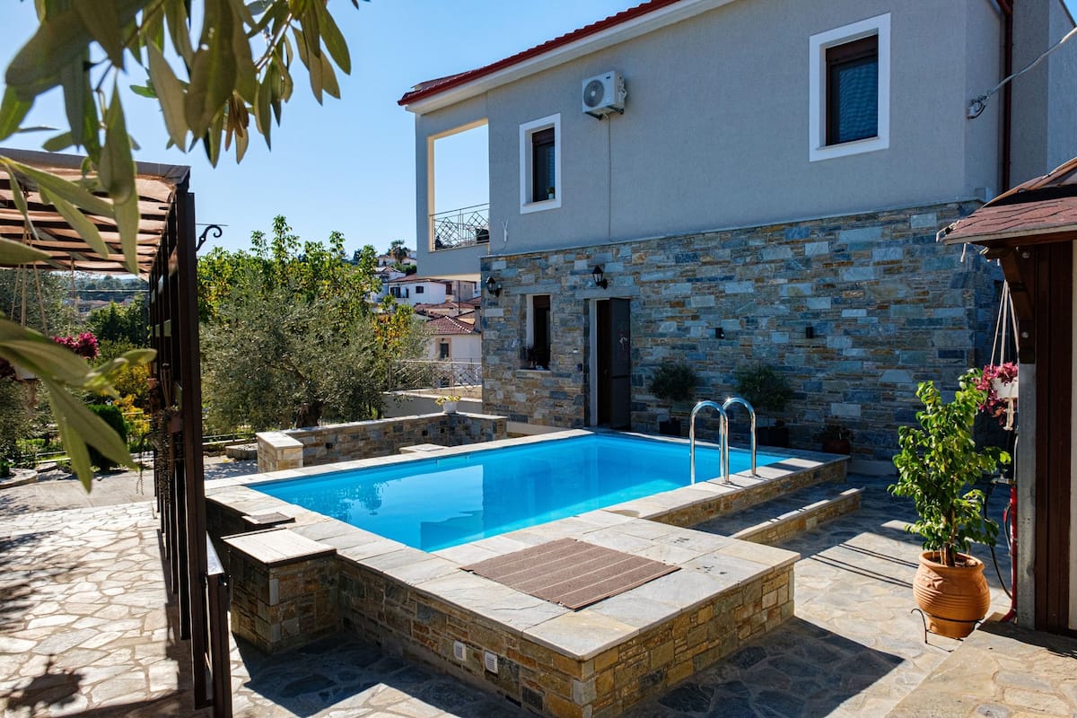 A swimming pool with stone tiles, a stone wall, and a pergola.