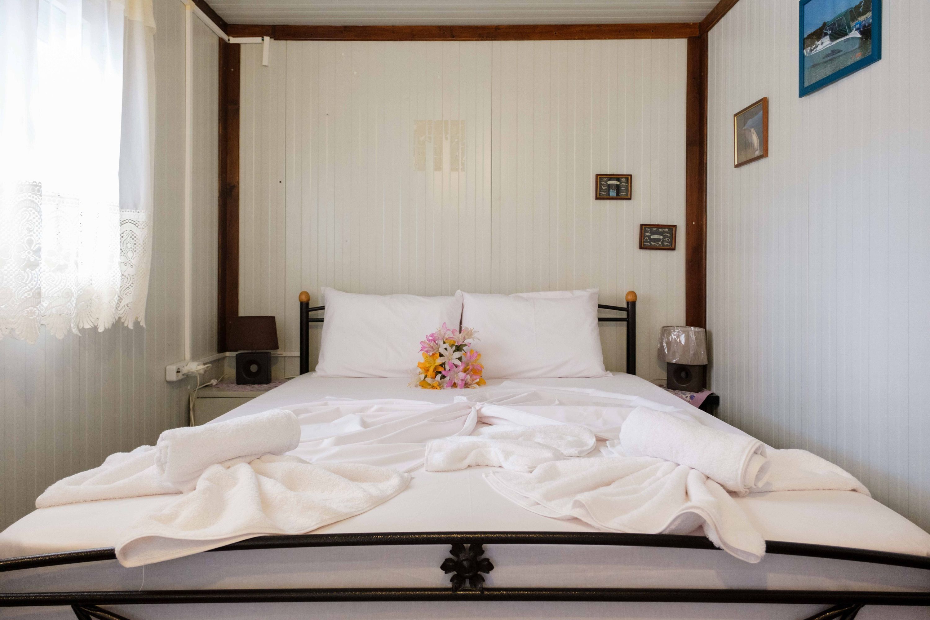 Una cama bien hecha con sábanas blancas, un ramo de flores y una mesita de noche con una lámpara.