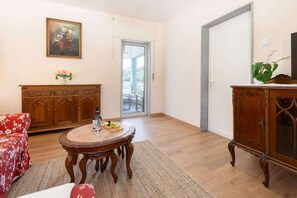 Ein Zimmer mit einem Holztisch, einem roten Blumensofa, einem Holzschrank und einem Gemälde an der Wand.