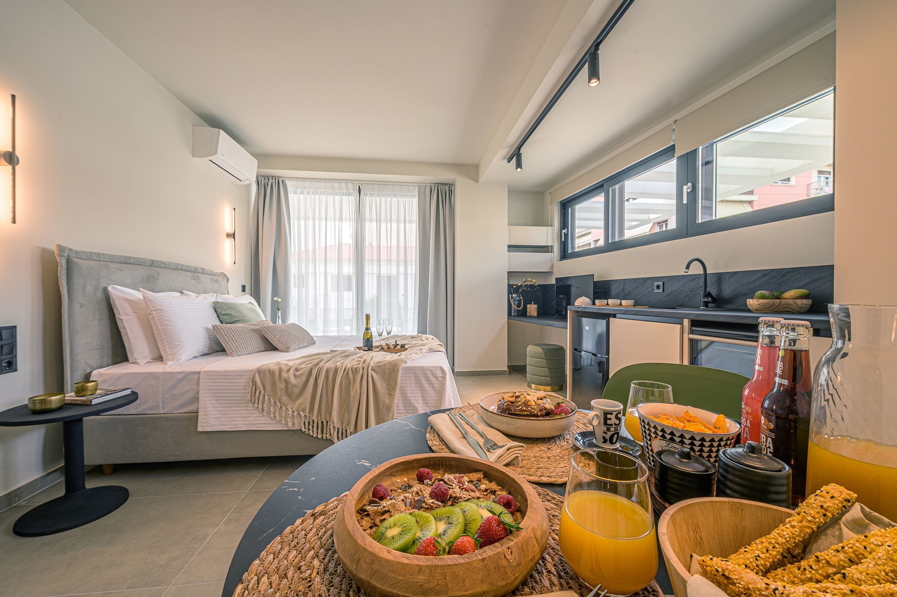 A modern hotel room with a bed, breakfast setup, and a kitchen area.