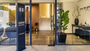 A modern hotel entrance with a glass door, a reception desk, and a staircase leading to the interior.