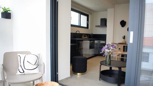 A modern kitchen with black appliances, a dining area with a round table and chairs, and a small stool. - Luaz Suites Volos Center (Volos)
