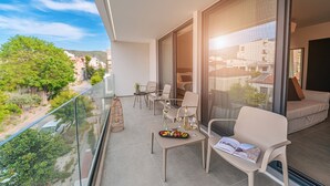 A balcony with a glass railing, outdoor seating, a table with a tray of fruit, and a book.