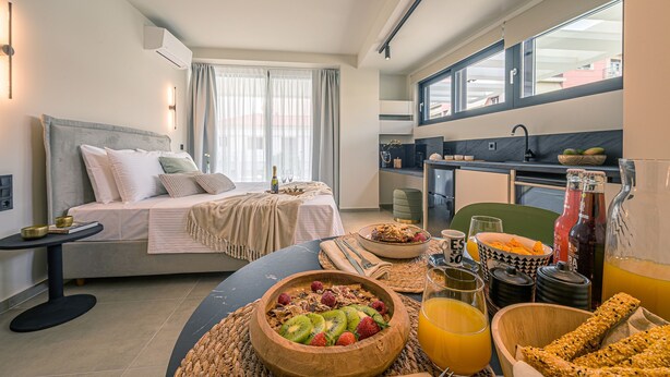 A modern hotel room with a bed, breakfast setup, and a kitchen area.